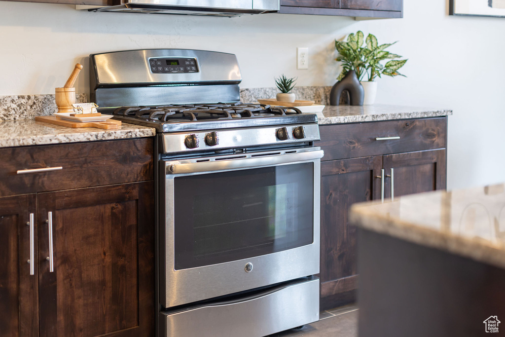 Kitchen with light stone counters, dark brown cabinetry, and stainless steel gas range oven