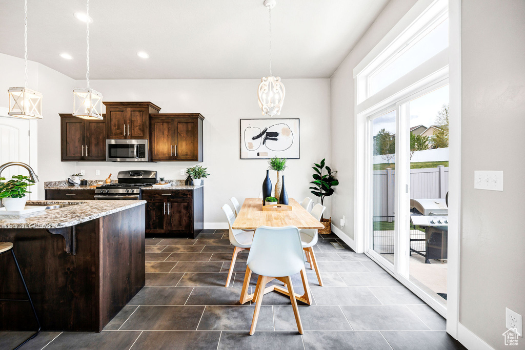 Kitchen with dark brown cabinets, light stone countertops, a sink, stainless steel appliances, and a kitchen bar