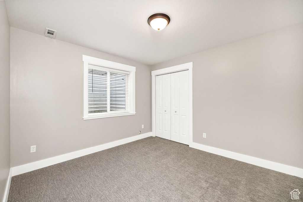 Unfurnished bedroom featuring baseboards, a closet, dark colored carpet, and visible vents