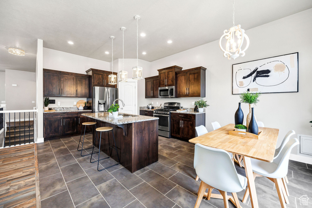 Kitchen with a kitchen island with sink, dark brown cabinetry, a breakfast bar, a chandelier, and appliances with stainless steel finishes