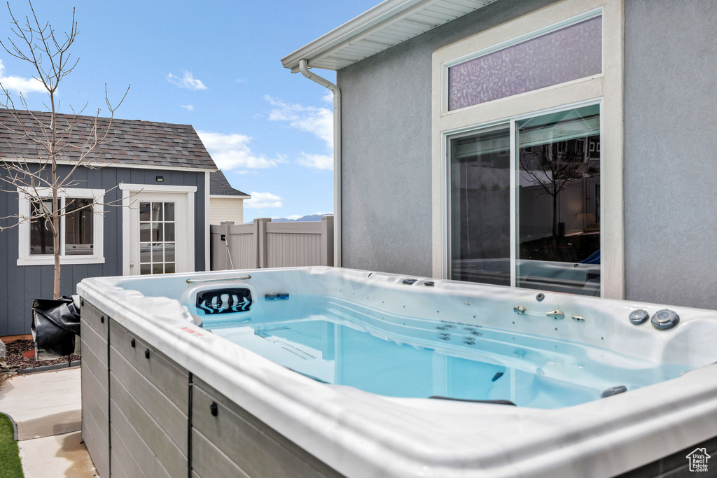 View of pool with a hot tub, fence, and an outbuilding