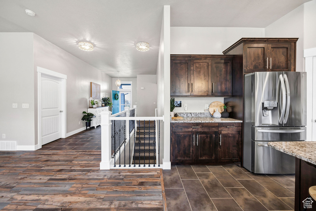 Kitchen with visible vents, dark brown cabinets, light stone countertops, stainless steel refrigerator with ice dispenser, and dark wood-type flooring