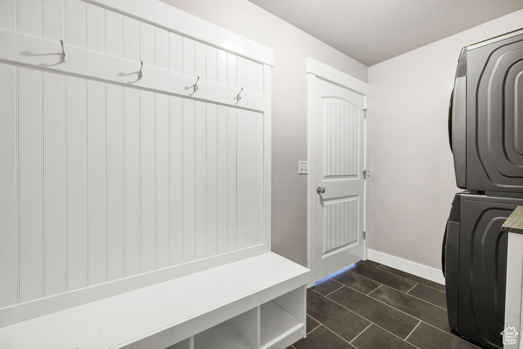 Clothes washing area with laundry area, a textured ceiling, stacked washing maching and dryer, baseboards, and dark tile patterned flooring