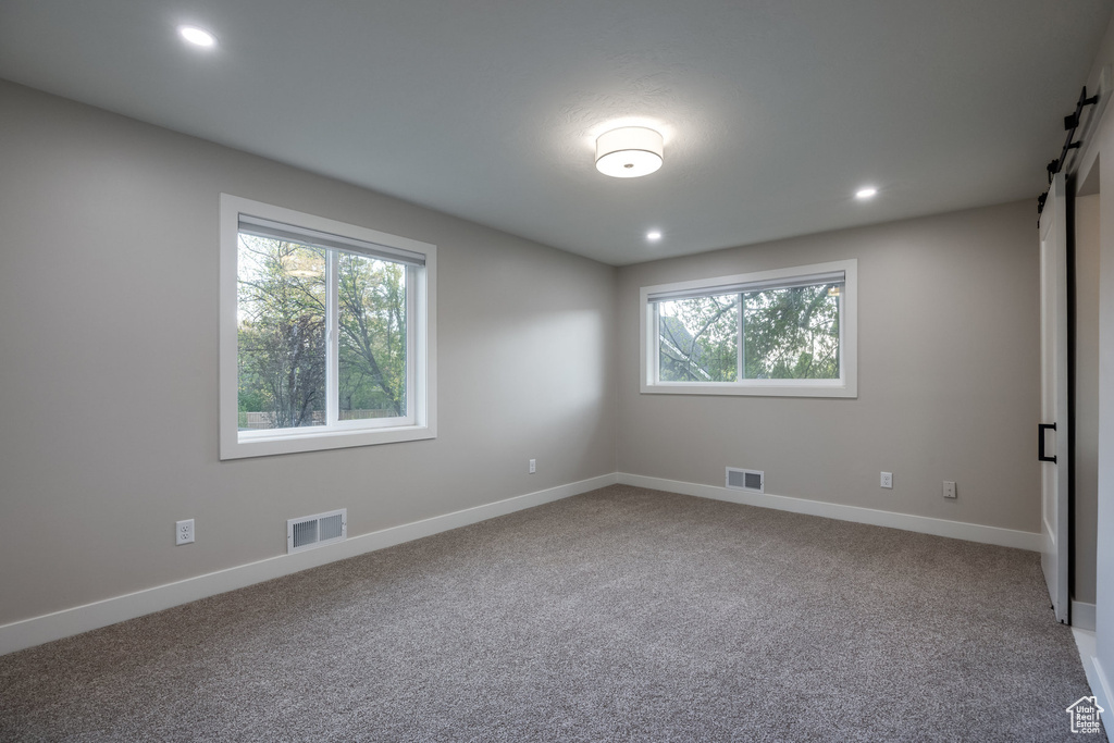 Carpeted spare room featuring visible vents, a barn door, and a wealth of natural light