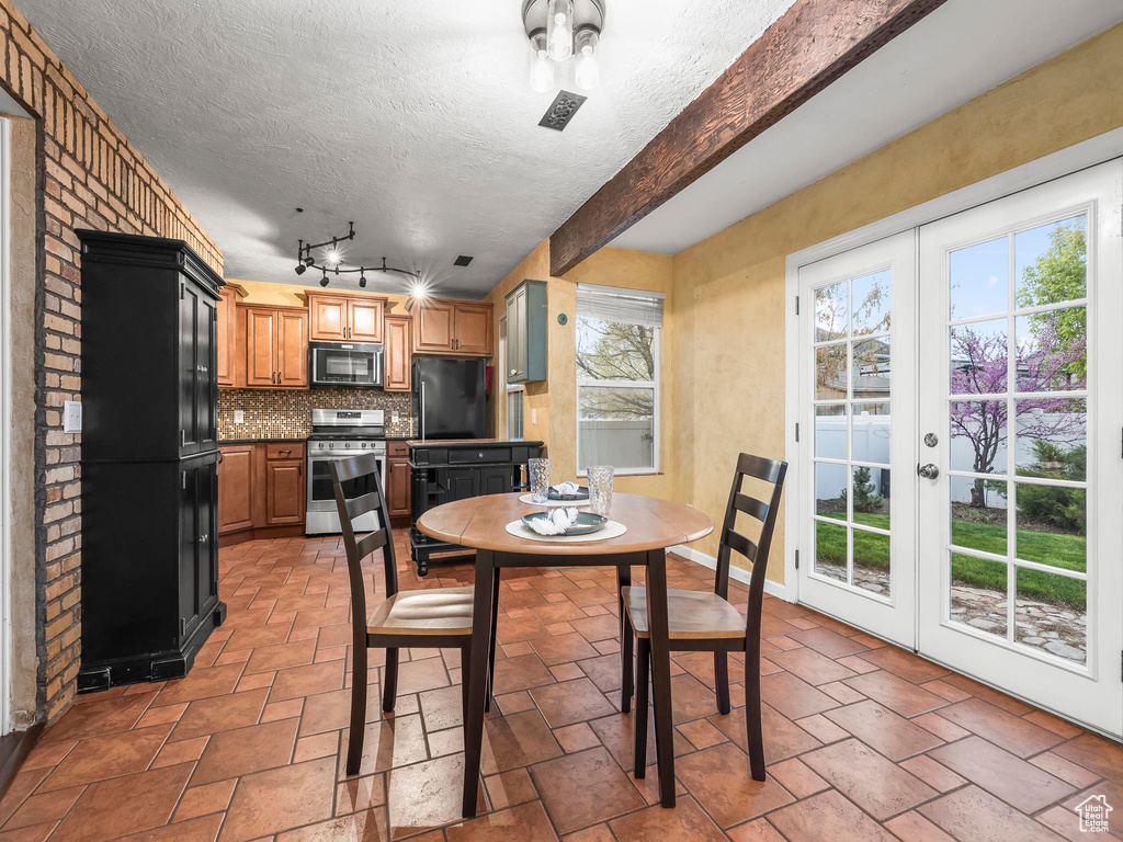Dining room with a textured ceiling, stone tile flooring, and beamed ceiling