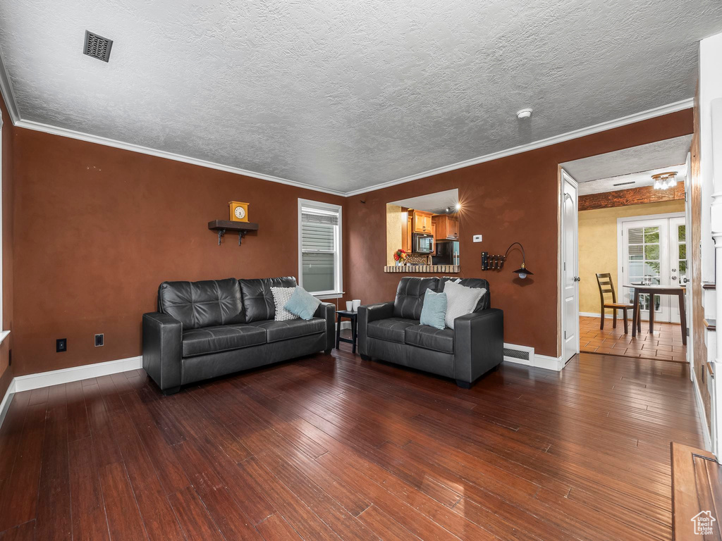 Living area featuring visible vents, baseboards, ornamental molding, and wood-type flooring