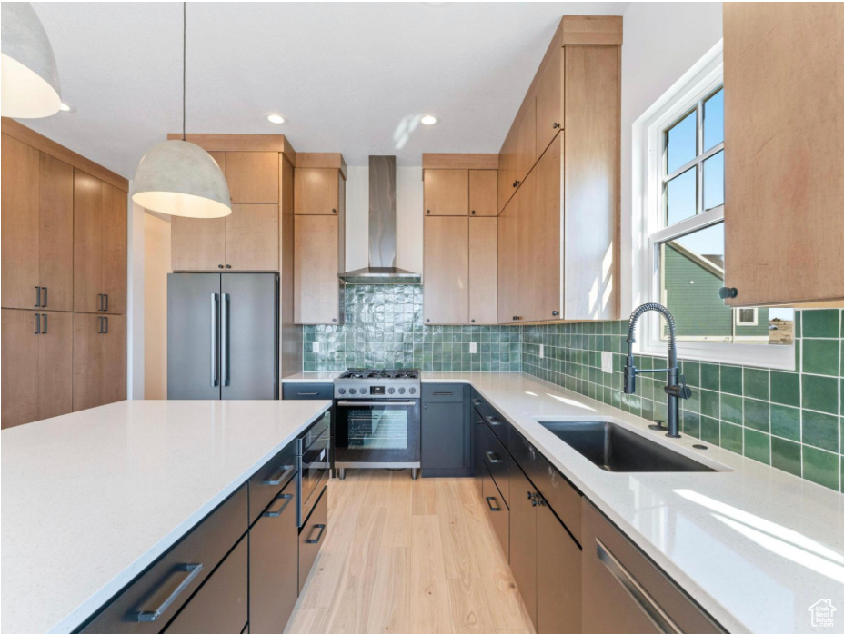 Kitchen with pendant lighting, wall chimney range hood, a sink, light wood-style flooring, and appliances with stainless steel finishes