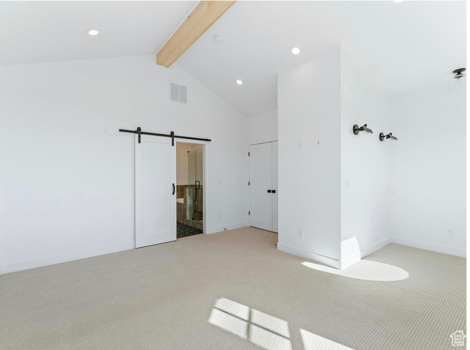 Unfurnished bedroom featuring visible vents, a barn door, light carpet, and beamed ceiling