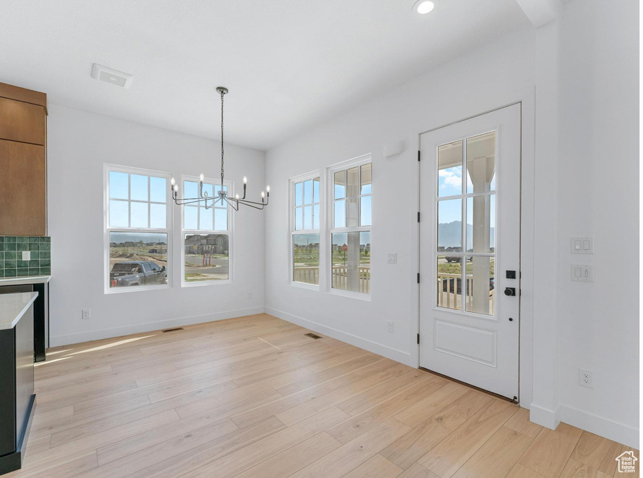 Unfurnished dining area featuring an inviting chandelier, light wood-style flooring, baseboards, and a healthy amount of sunlight
