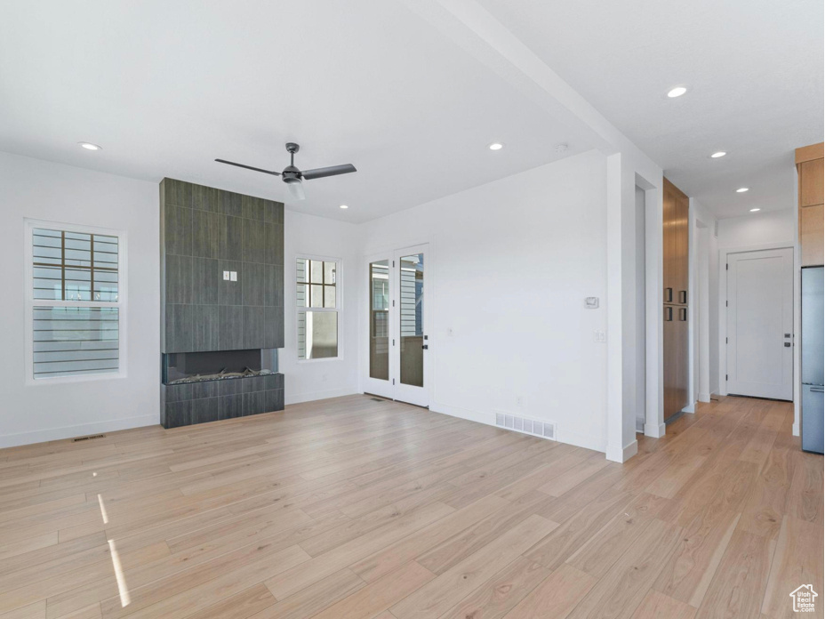 Unfurnished living room featuring a tiled fireplace, a wealth of natural light, light wood-type flooring, and visible vents