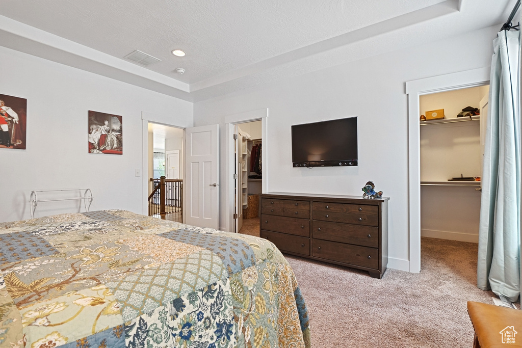 Carpeted bedroom with a walk in closet, baseboards, a tray ceiling, visible vents, and a closet