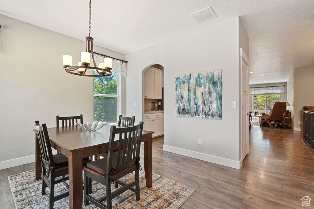 Dining space with arched walkways, a chandelier, baseboards, wood finished floors, and visible vents
