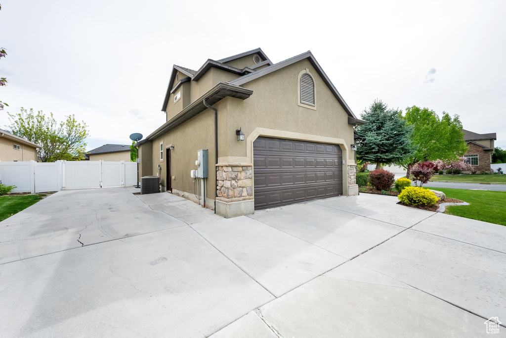 View of home's exterior with a garage, stone siding, stucco siding, central AC unit, and concrete driveway