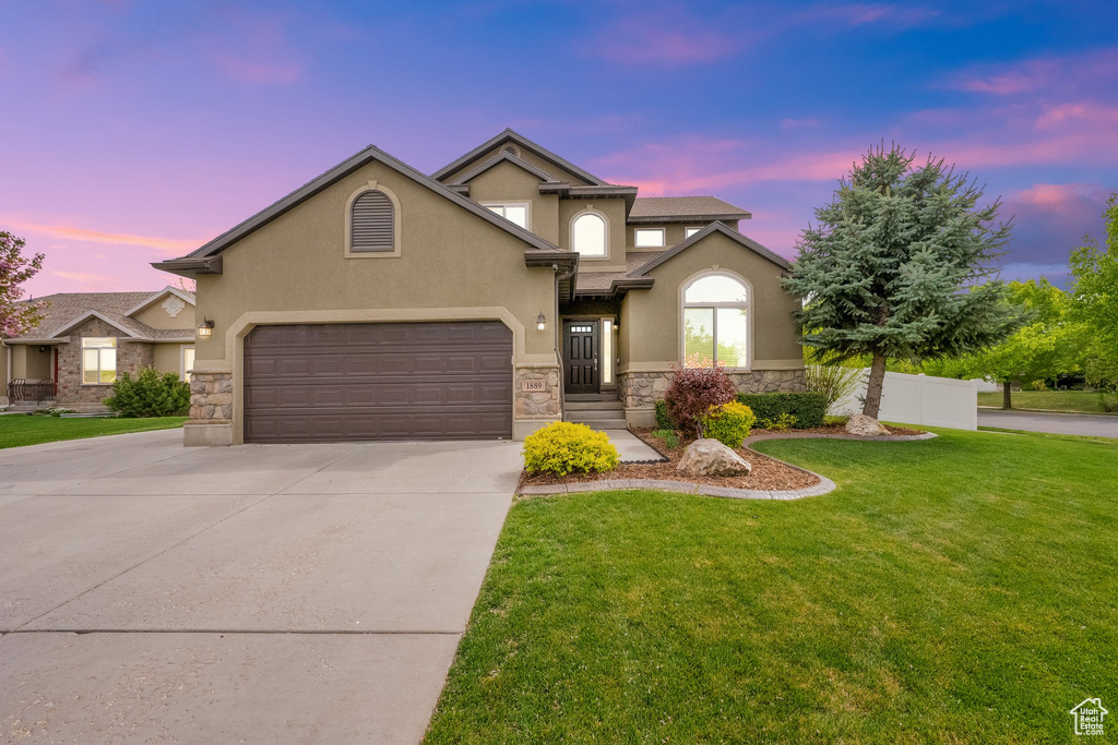 View of front of house with a front lawn, stucco siding, stone siding, and concrete driveway
