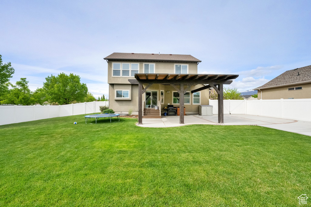 Rear view of house with a trampoline, stucco siding, a fenced backyard, a patio area, and a lawn