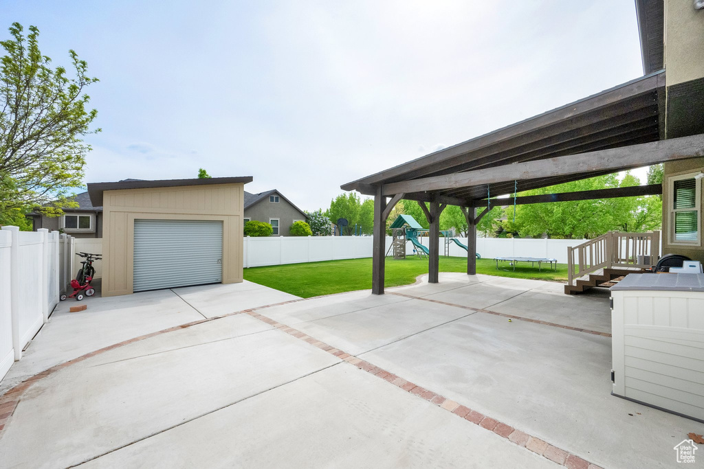 View of patio / terrace with a fenced backyard, a playground, an outbuilding, and concrete driveway