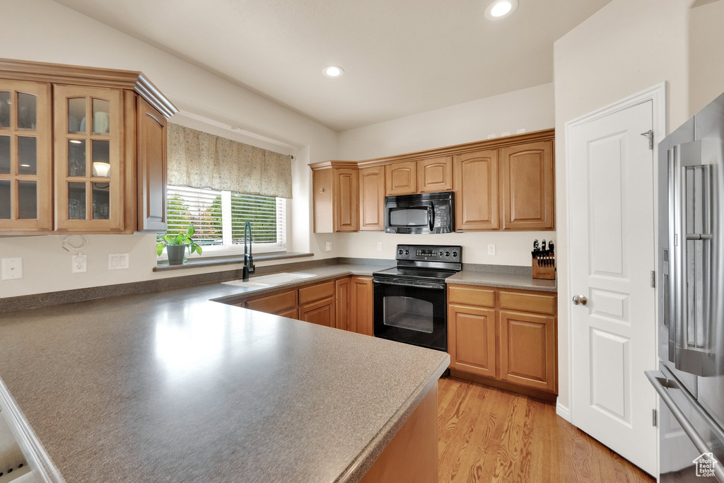 Kitchen featuring a sink, black appliances, a peninsula, glass insert cabinets, and recessed lighting