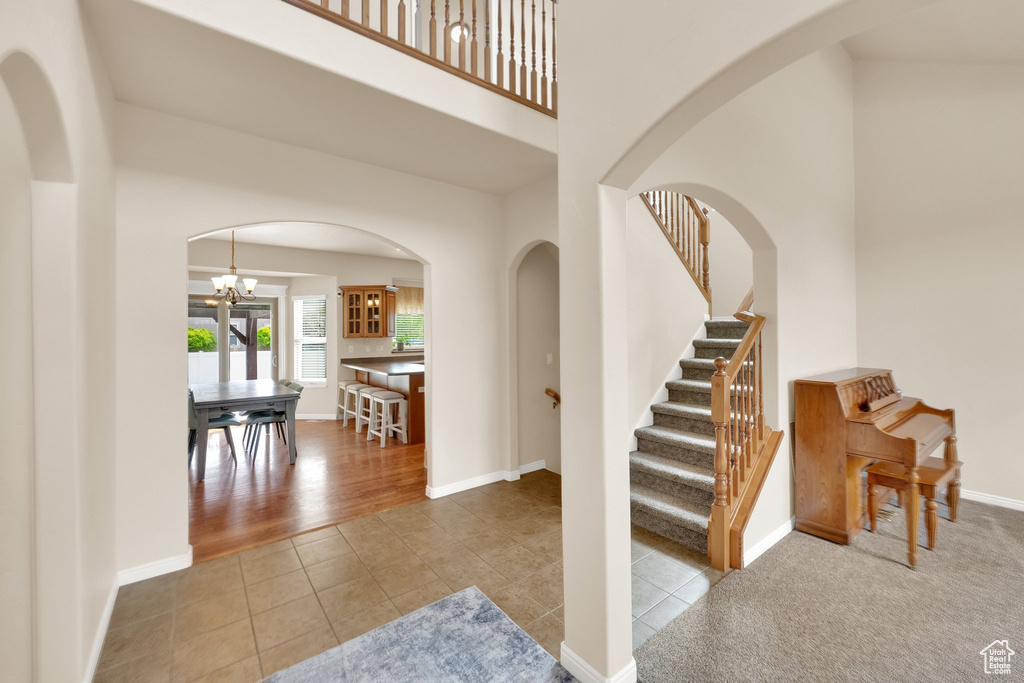 Staircase featuring arched walkways, tile patterned floors, a chandelier, baseboards, and a towering ceiling