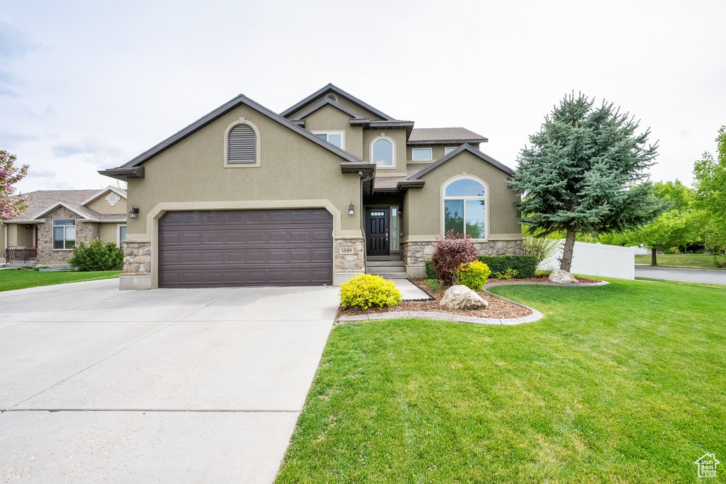 View of front facade with stucco siding, driveway, a front lawn, and stone siding