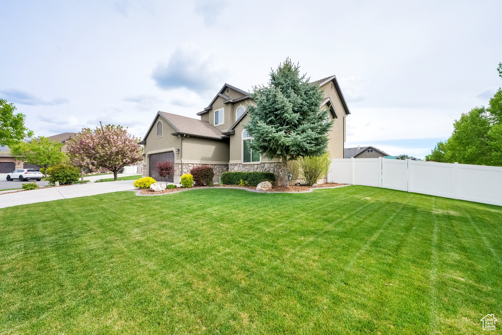 View of front of property featuring driveway, a front yard, fence, stone siding, and stucco siding