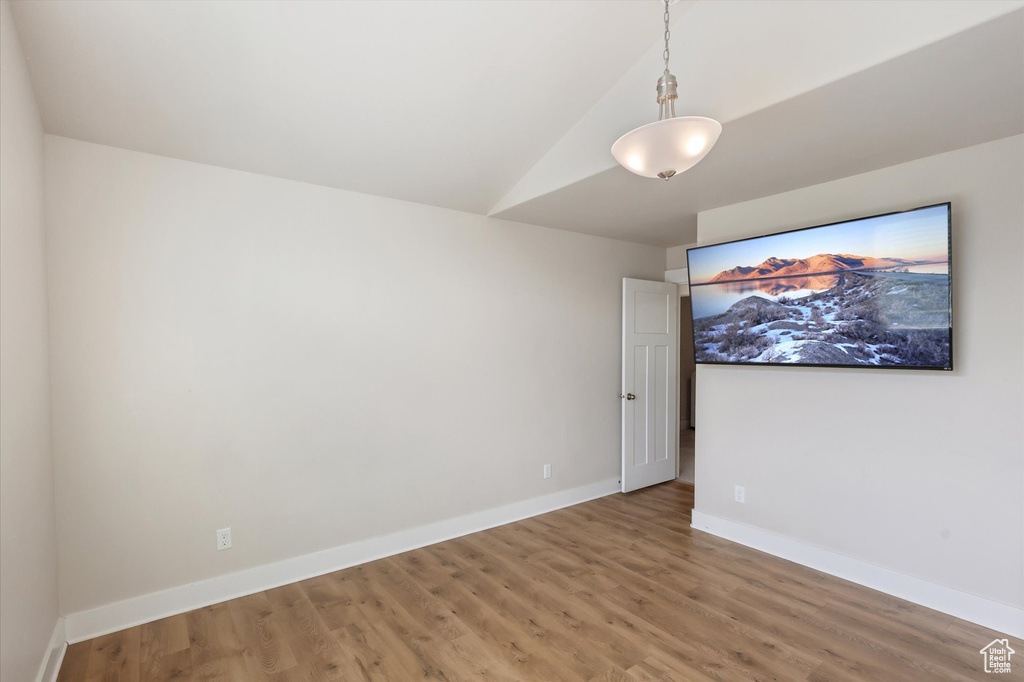 Spare room with baseboards, light wood-style flooring, and lofted ceiling