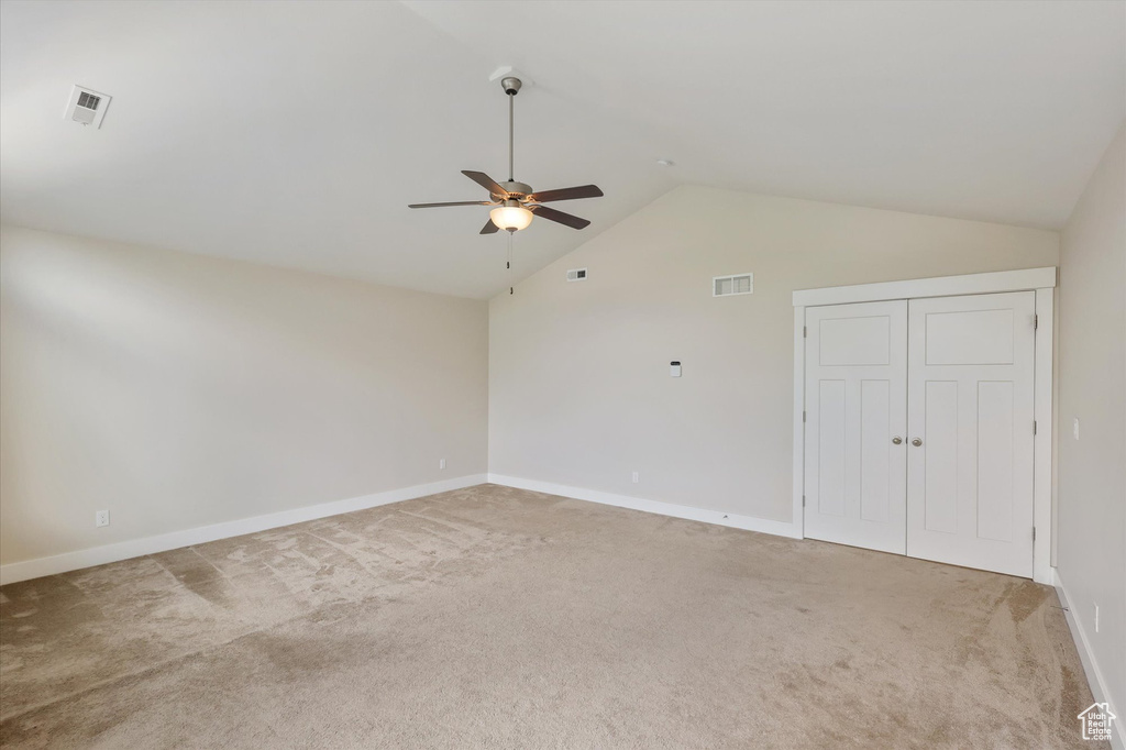 Unfurnished room featuring light colored carpet, a ceiling fan, baseboards, vaulted ceiling, and visible vents