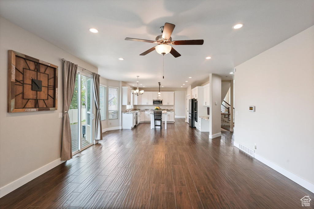 Unfurnished living room featuring dark wood-style flooring, stairway, baseboards, and ceiling fan with notable chandelier
