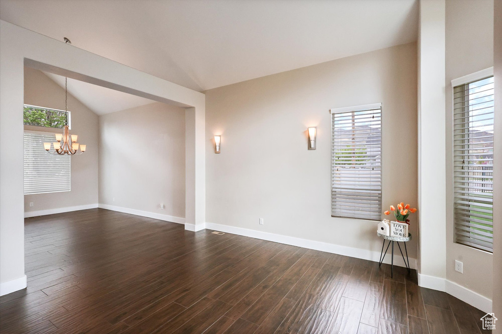 Spare room featuring an inviting chandelier, plenty of natural light, vaulted ceiling, and dark wood-style floors