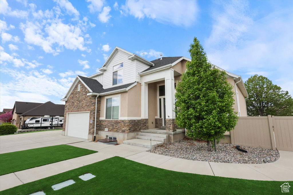 View of front of home with a front lawn, fence, stone siding, stucco siding, and concrete driveway