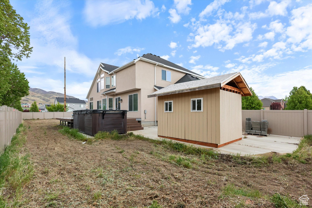 Back of house with a fenced backyard, an outdoor structure, a hot tub, and a patio area