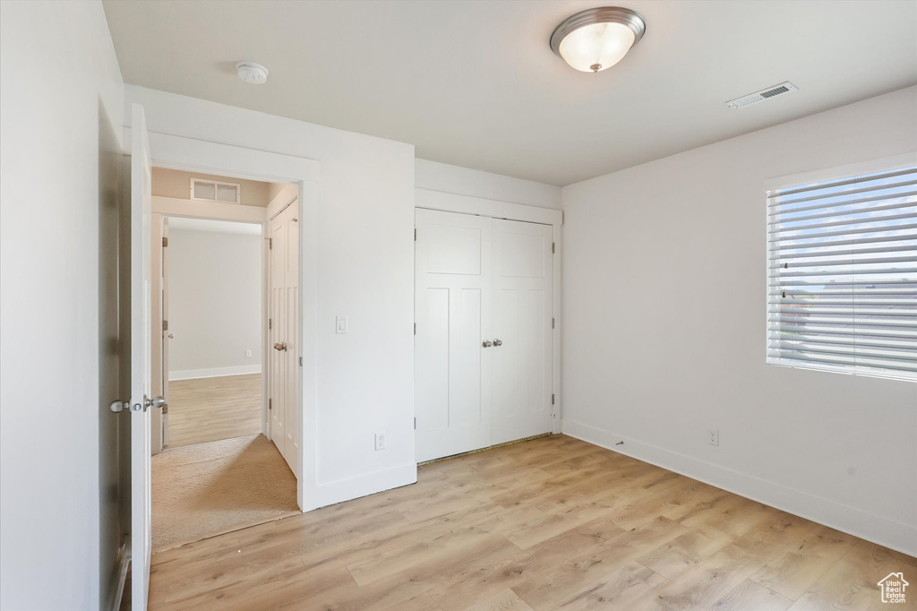 Unfurnished bedroom with baseboards, light wood-style floors, visible vents, and a closet