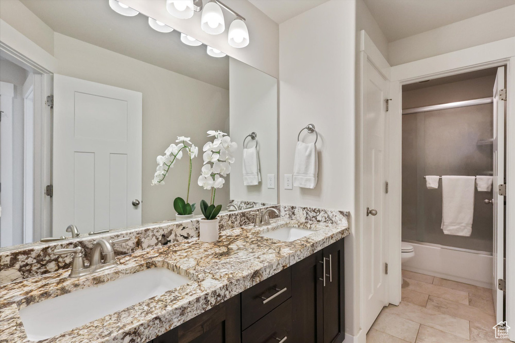 Full bath featuring a sink, enclosed tub / shower combo, toilet, and double vanity