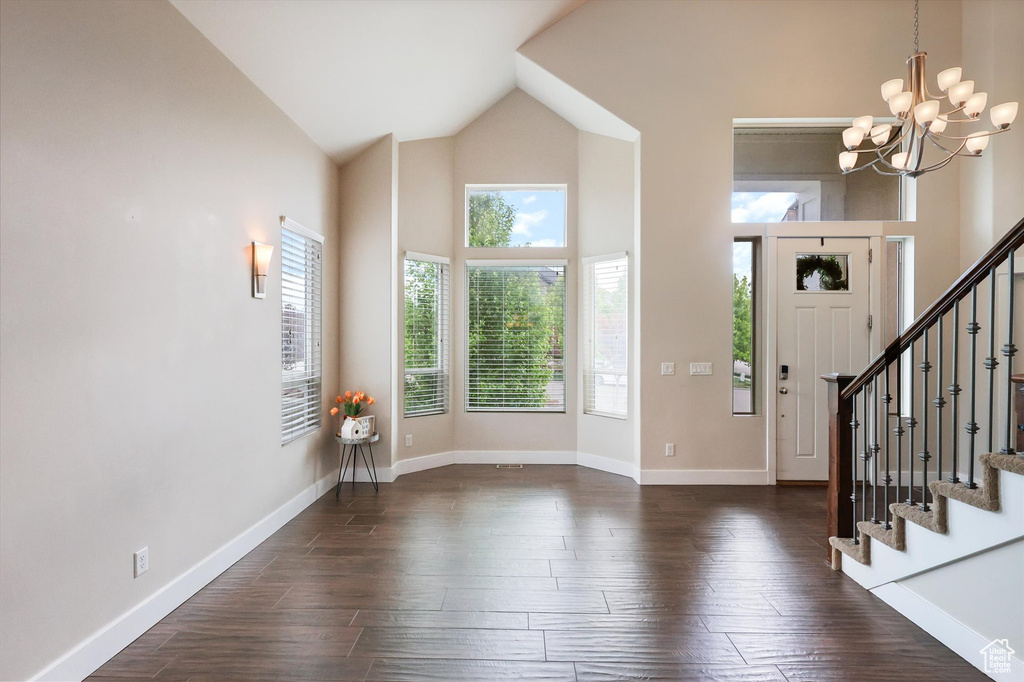 Entrance foyer featuring an inviting chandelier, stairs, baseboards, high vaulted ceiling, and dark wood-type flooring