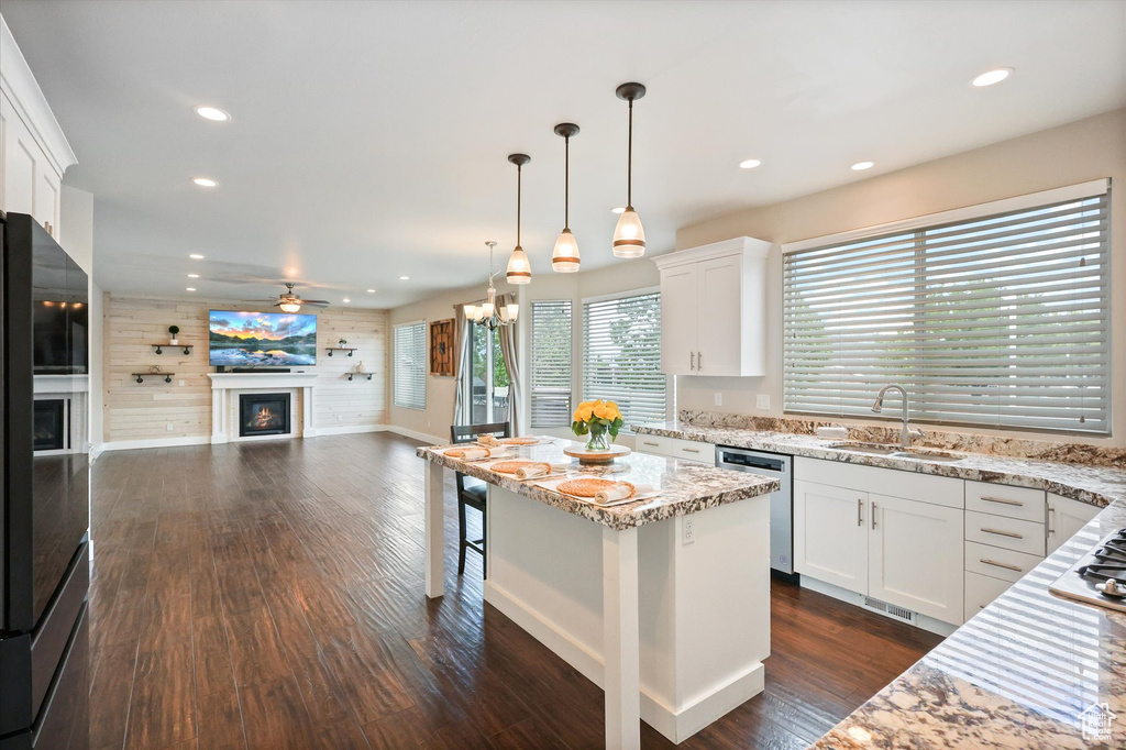 Kitchen with appliances with stainless steel finishes, light stone counters, a sink, a glass covered fireplace, and recessed lighting