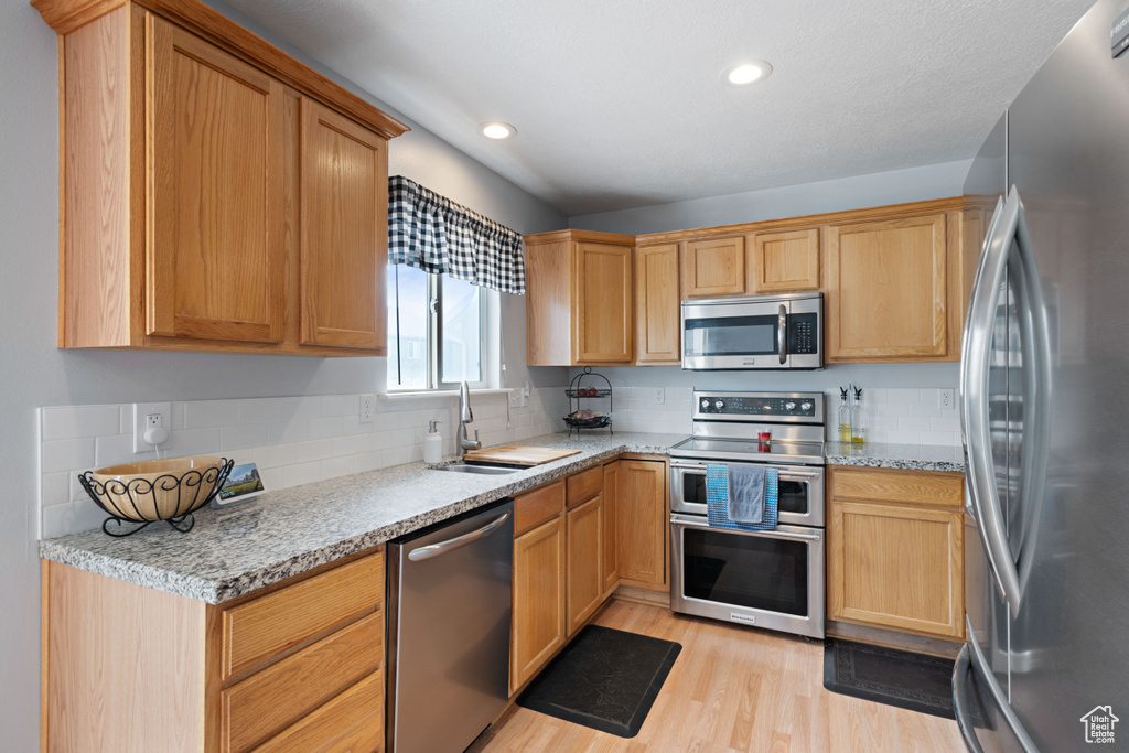 Kitchen featuring appliances with stainless steel finishes, tasteful backsplash, a sink, light wood-style floors, and recessed lighting