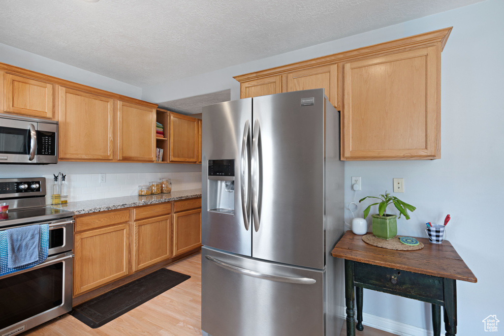 Kitchen with a textured ceiling, open shelves, light wood-type flooring, light stone counters, and stainless steel appliances