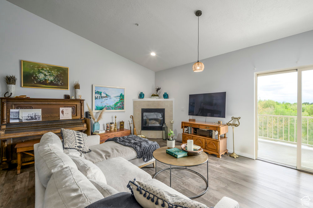 Living room with vaulted ceiling, wood finished floors, a tile fireplace, baseboards, and recessed lighting