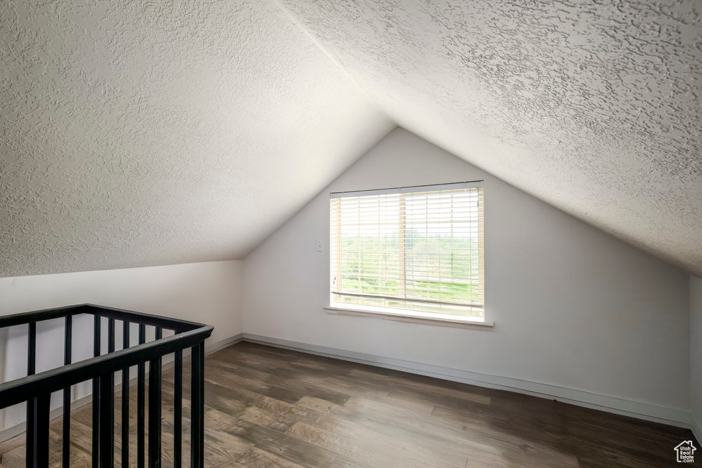 Bonus room with baseboards, vaulted ceiling, a textured ceiling, and wood finished floors