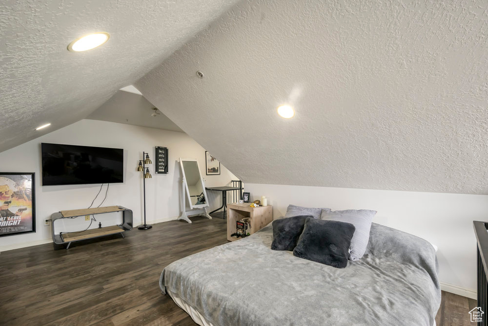 Bedroom featuring wood finished floors, baseboards, a textured ceiling, and lofted ceiling