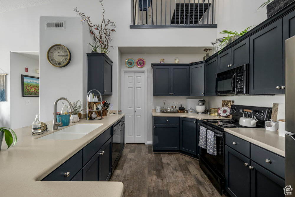 Kitchen with visible vents, light countertops, a sink, dark wood finished floors, and black appliances