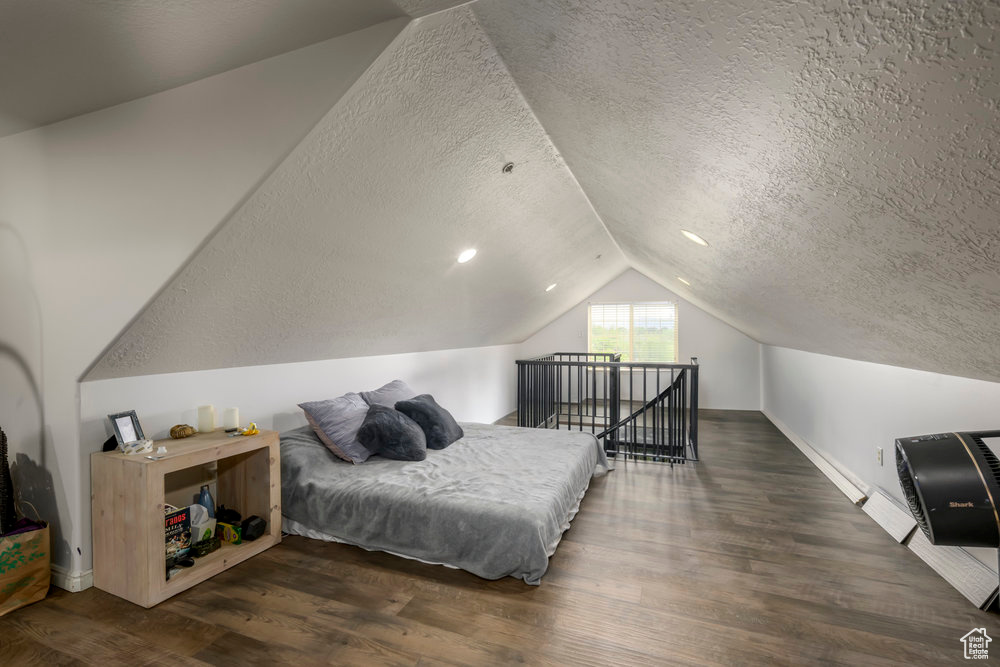 Bedroom featuring baseboards, a textured ceiling, wood finished floors, and lofted ceiling