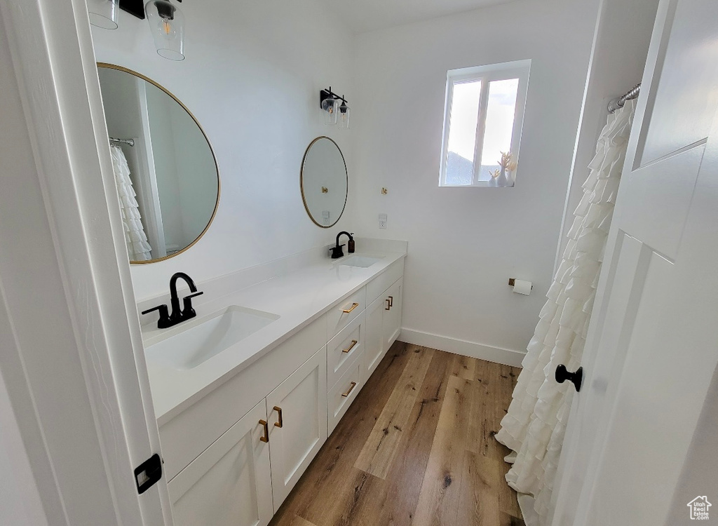 Full bathroom featuring double vanity, a sink, baseboards, and wood finished floors