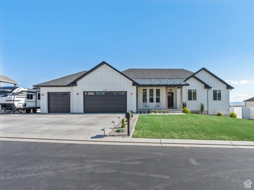 Modern farmhouse with a front lawn, fence, board and batten siding, concrete driveway, and an attached garage