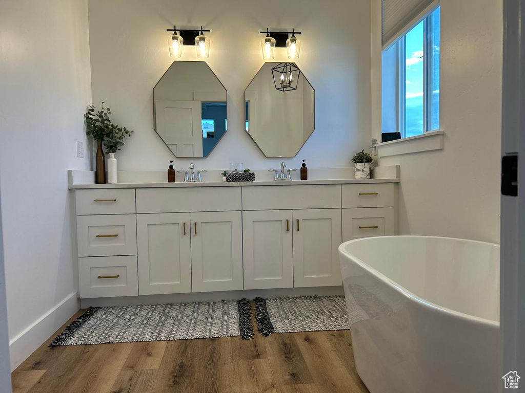 Bathroom featuring double vanity, a freestanding tub, wood finished floors, a sink, and baseboards