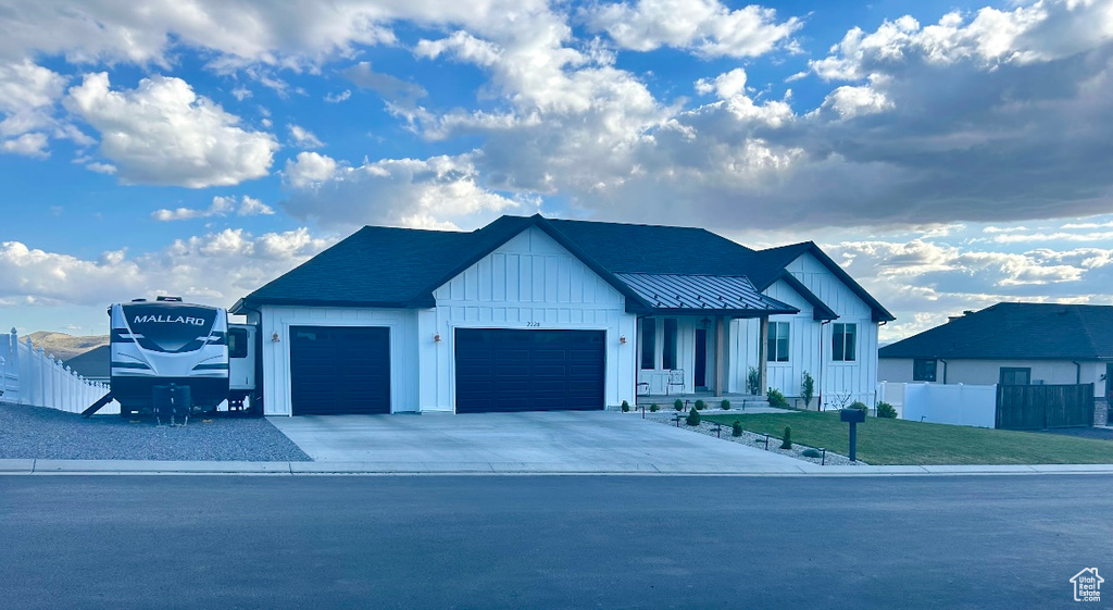 Modern inspired farmhouse with board and batten siding, driveway, fence, a front lawn, and an attached garage