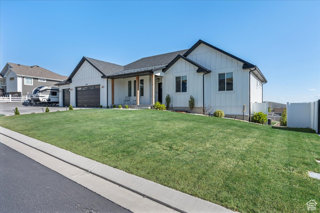 View of front of home with a garage, fence, board and batten siding, and a front lawn