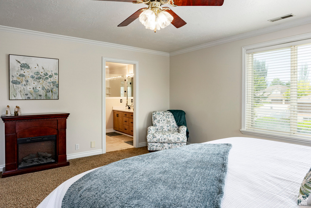 Carpeted bedroom featuring ornamental molding, a fireplace, baseboards, a ceiling fan, and ensuite bath
