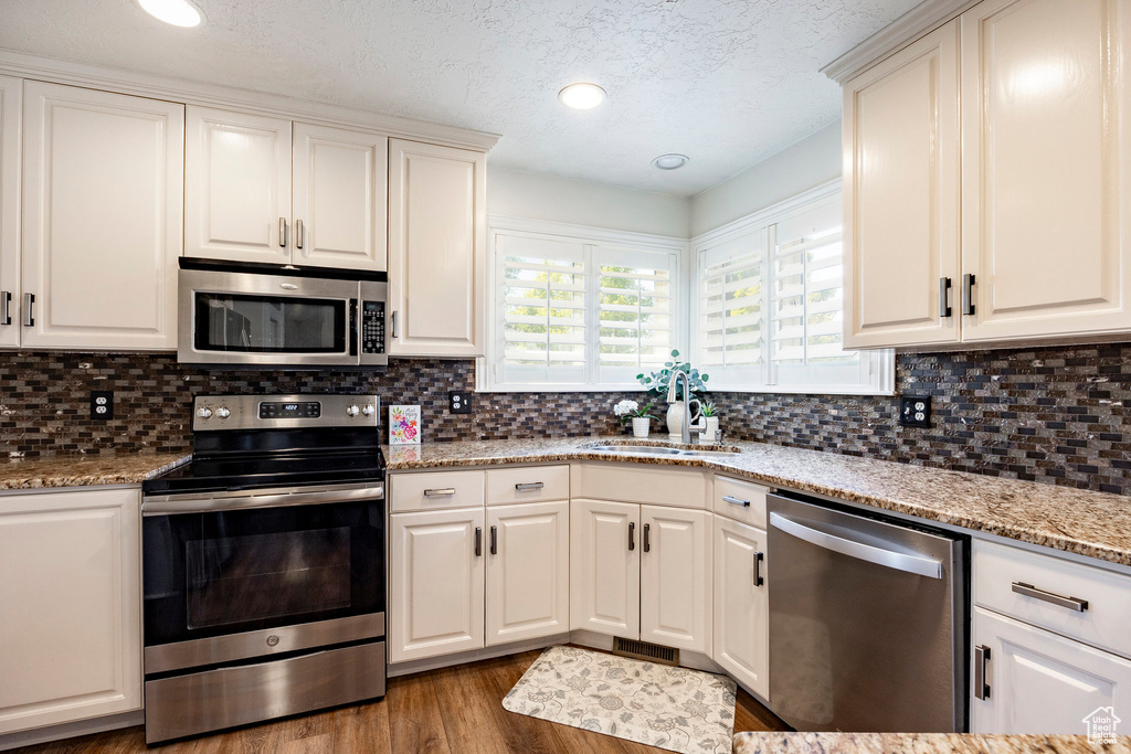 Kitchen with stainless steel appliances, a sink, wood finished floors, decorative backsplash, and a textured ceiling