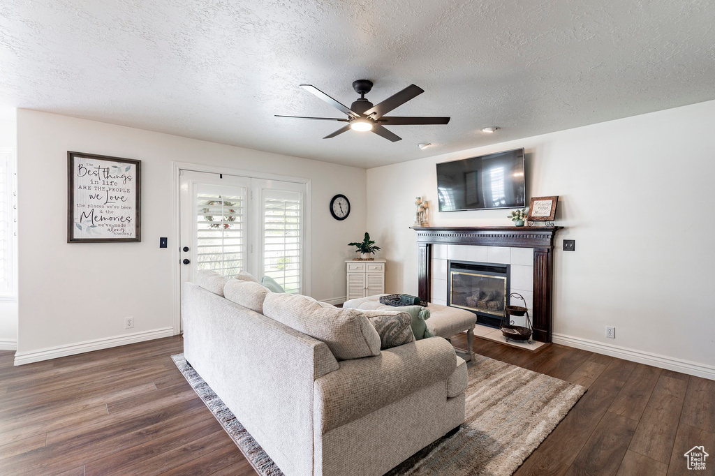 Living area featuring dark wood-style flooring, baseboards, a textured ceiling, a tiled fireplace, and a ceiling fan