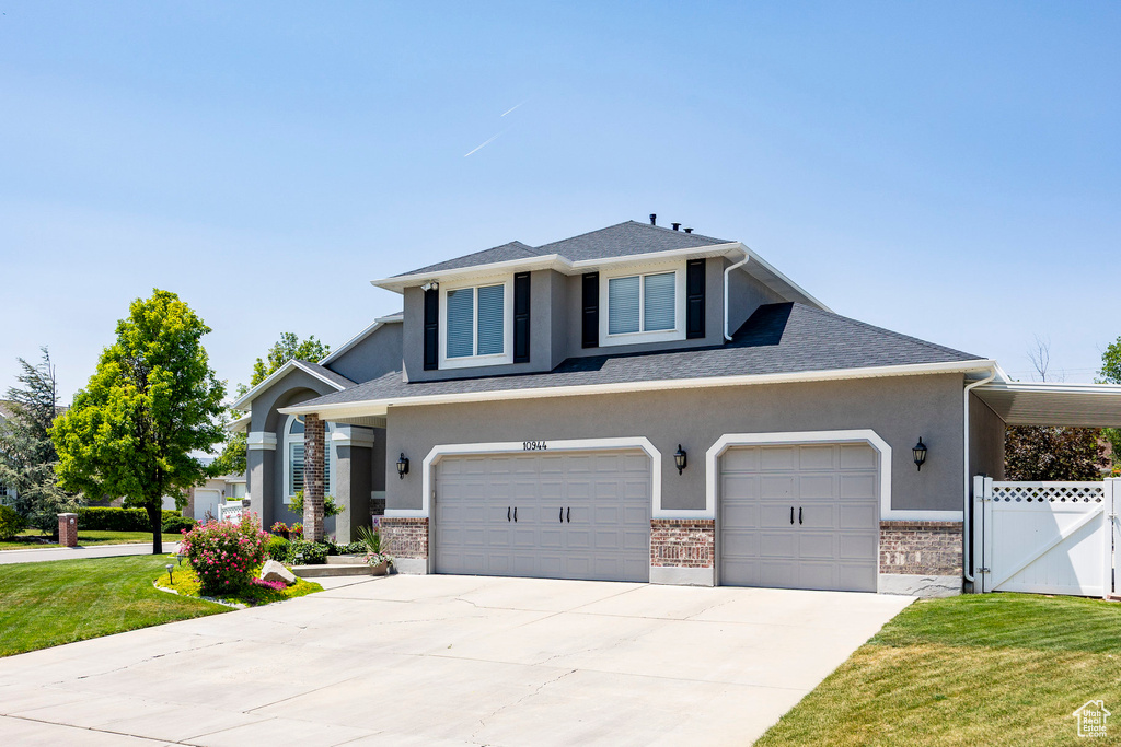 View of front of home with stucco siding, concrete driveway, brick siding, and a gate
